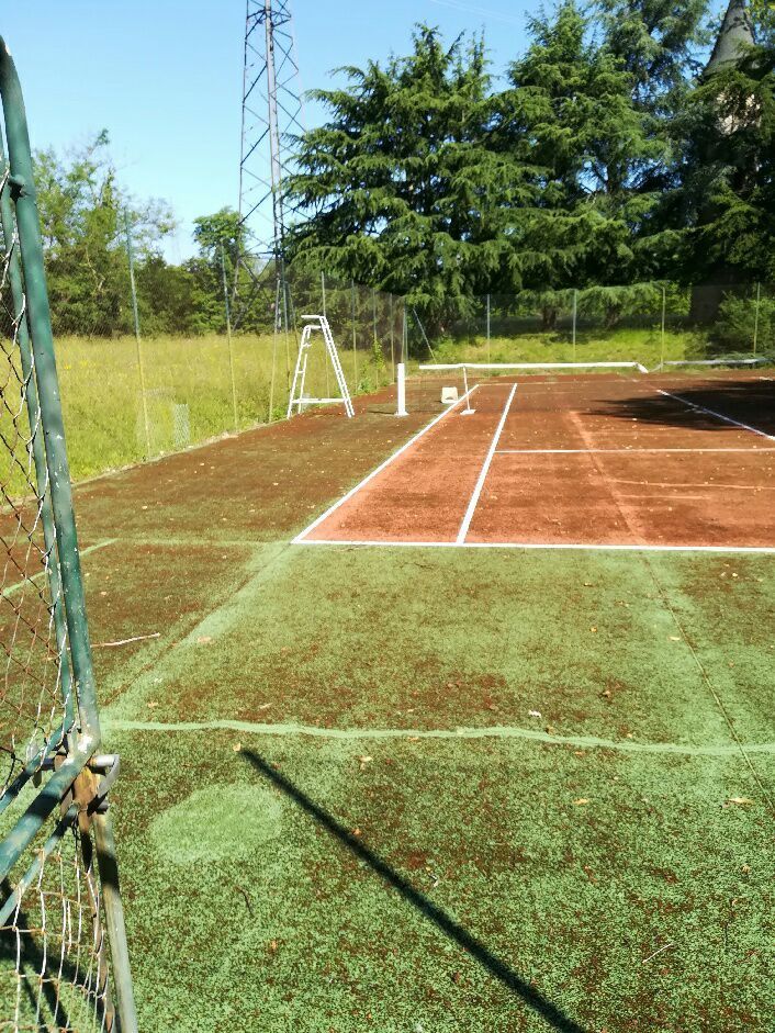 Terrain de cricket par une journée ensoleillée, avec du gazon artificiel vert et en arrière-plan des arbres et un poteau électrique.