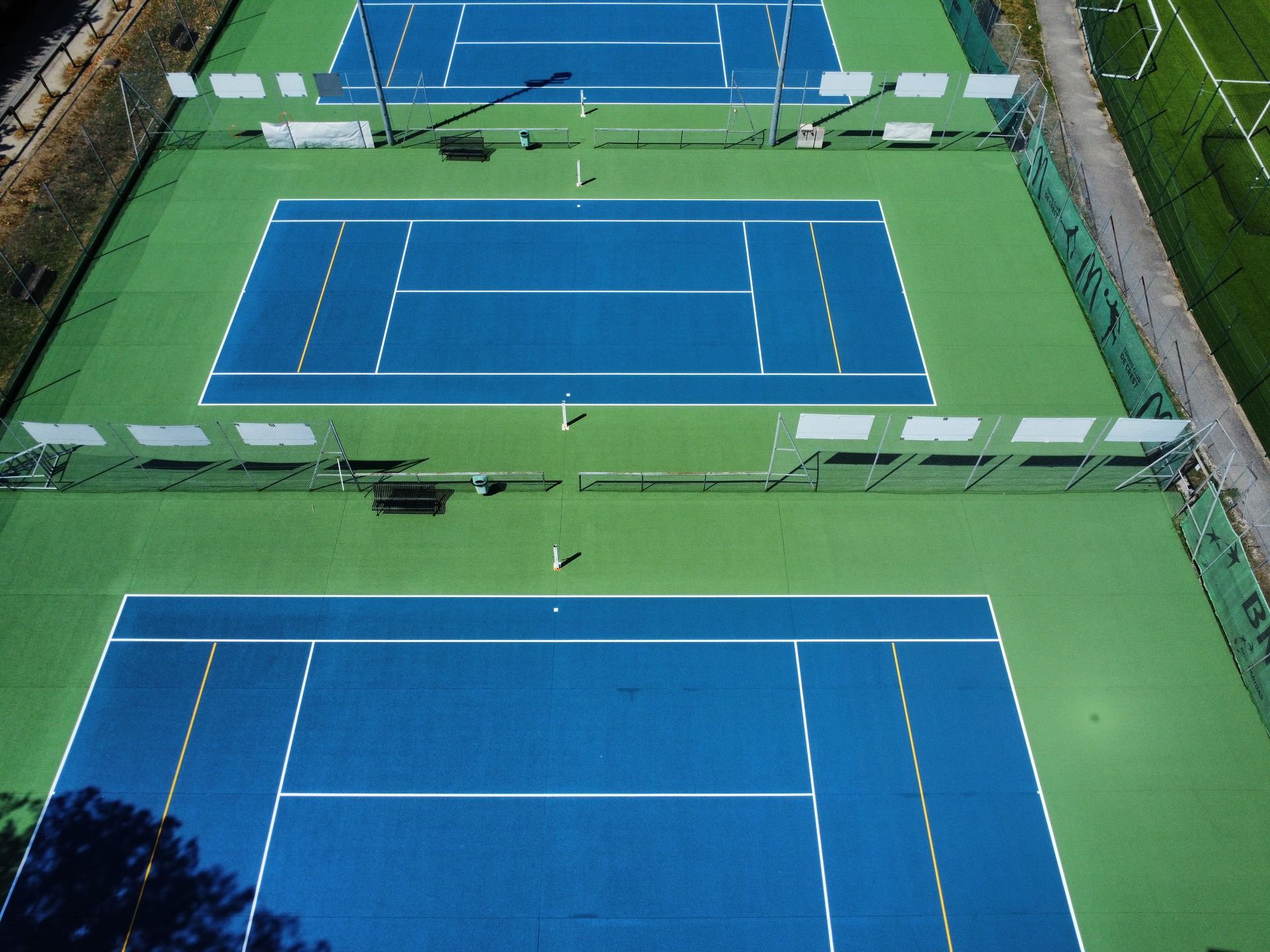 Vue aérienne de trois courts de tennis bleus entourés de gazon vert.