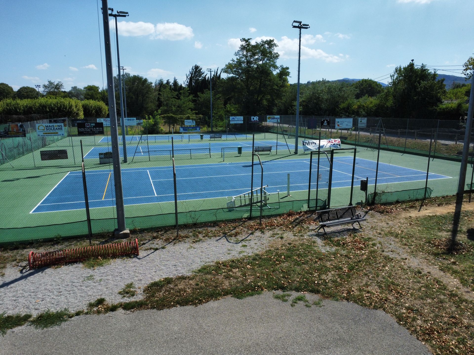 Vue aérienne de courts de tennis bleus et verts, entourés d'arbres.