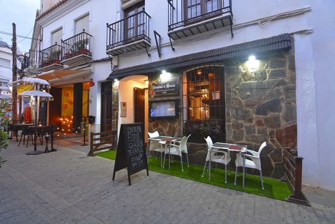 Terraza de café al aire libre junto a un edificio blanco con mesas, sillas y una pizarra de menú iluminada al atardecer.