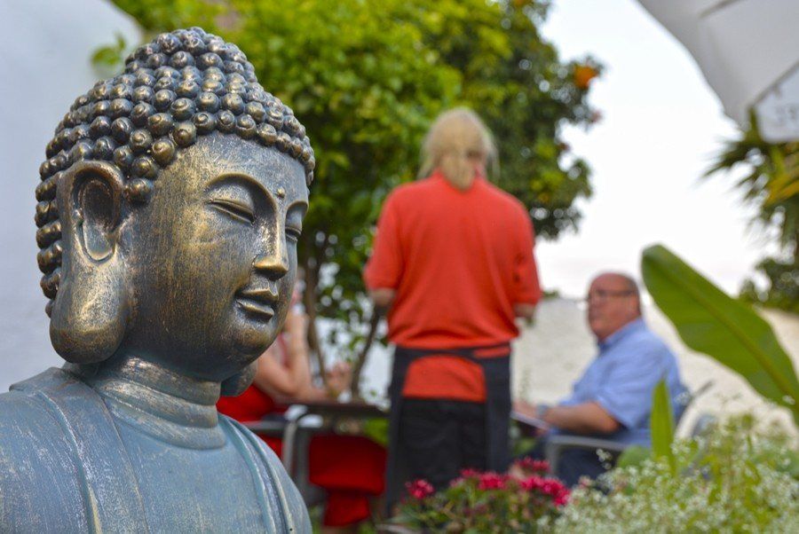 Estatua de Buda en primer plano con gente charlando en un jardín detrás.