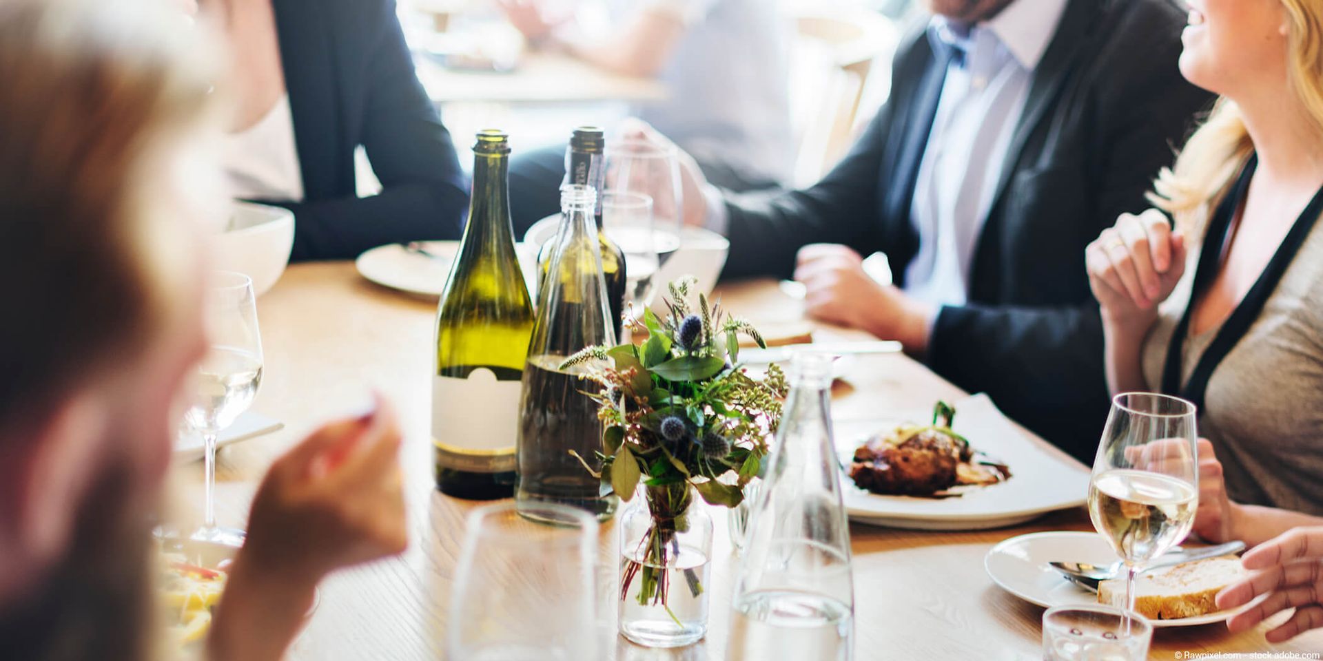 Menschen an einem Restauranttisch, mit Weinflaschen, Essen und Gläsern.