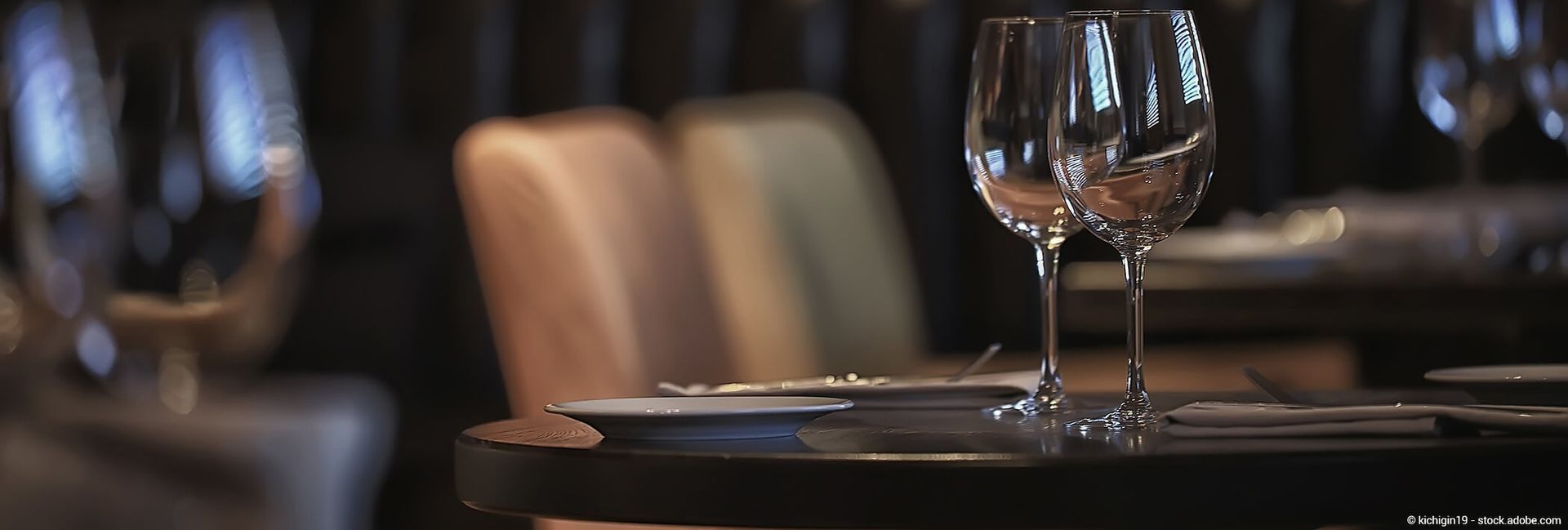 Zwei Weingläser auf einem zum Abendessen gedeckten Tisch; Stühle sind im Hintergrund zu sehen.