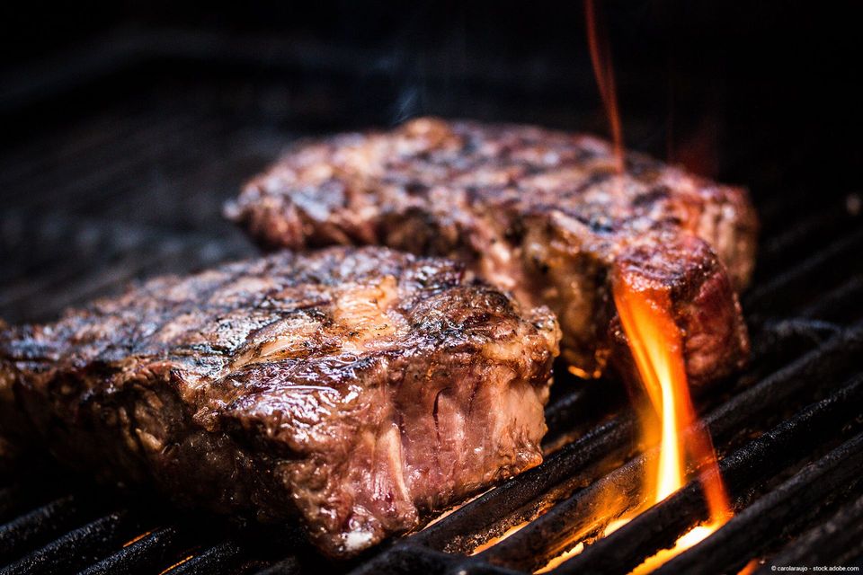 Zwei Steaks grillen auf einem heißen Grill mit Flammen.