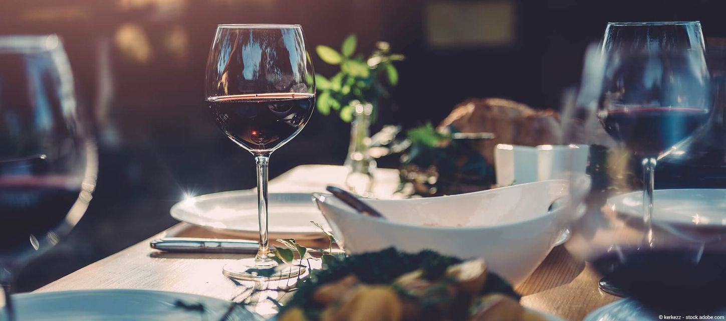 Ein Tisch mit Gläsern Rotwein, weißen Schüsseln und Tellern vor verschwommenem Hintergrund.