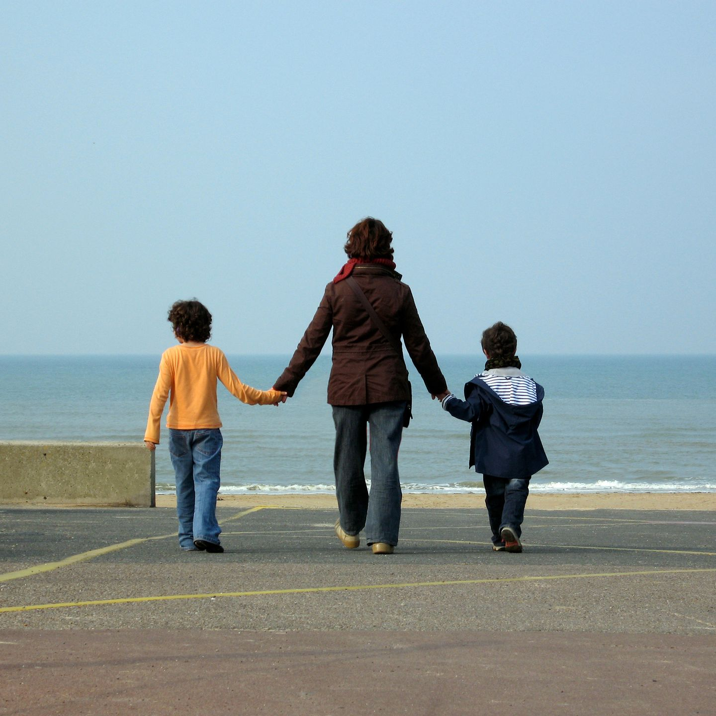 Une personne tient la main de deux enfants qui marchent vers la plage.