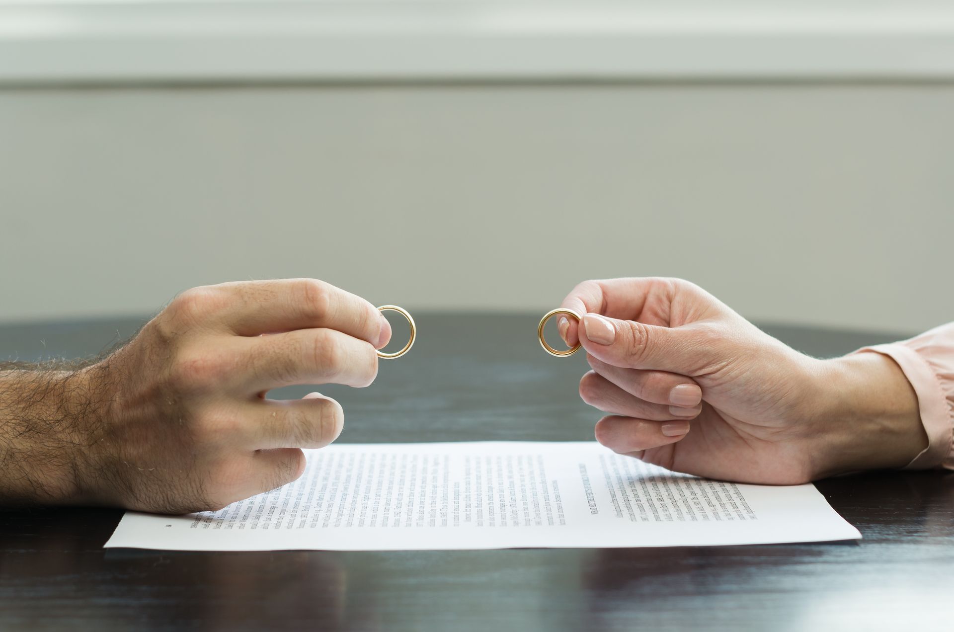 Des mains tenant des alliances au-dessus d'un document de divorce posé sur une table.