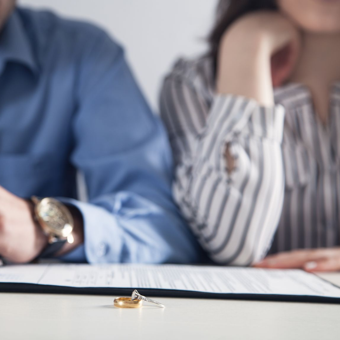 Des alliances sur une table, avec un couple en arrière-plan qui semble bouleversé, signant peut-être des papiers de divorce.