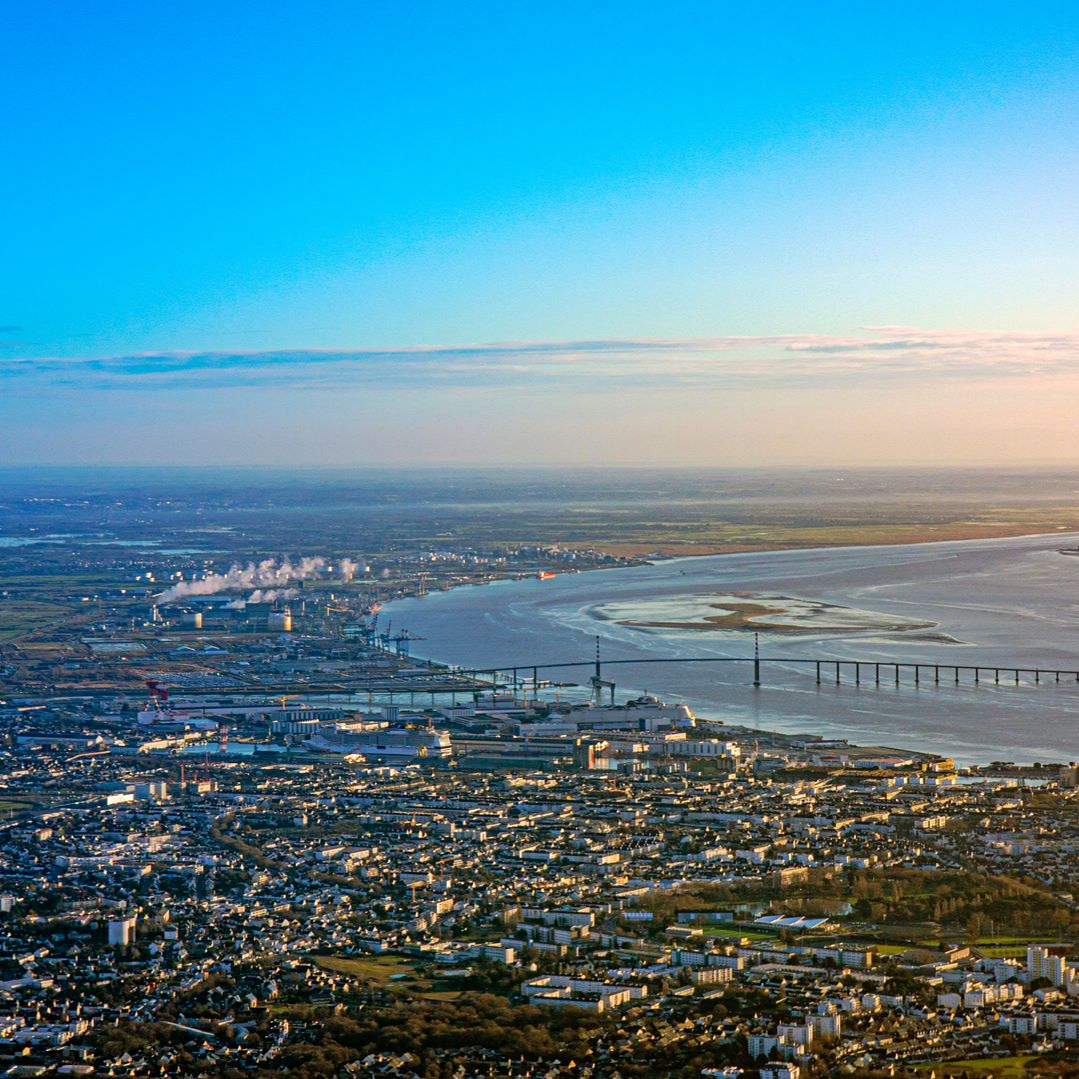 Vue aérienne d'une ville bordant un large fleuve et l'océan. Ciel d'un bleu éclatant avec un lever de soleil.