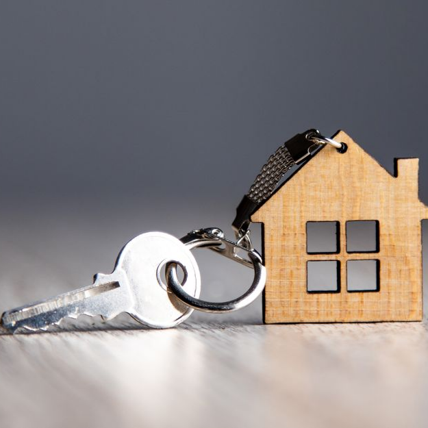 Porte-clés en forme de clé et de maison sur une surface en bois, sur fond gris.