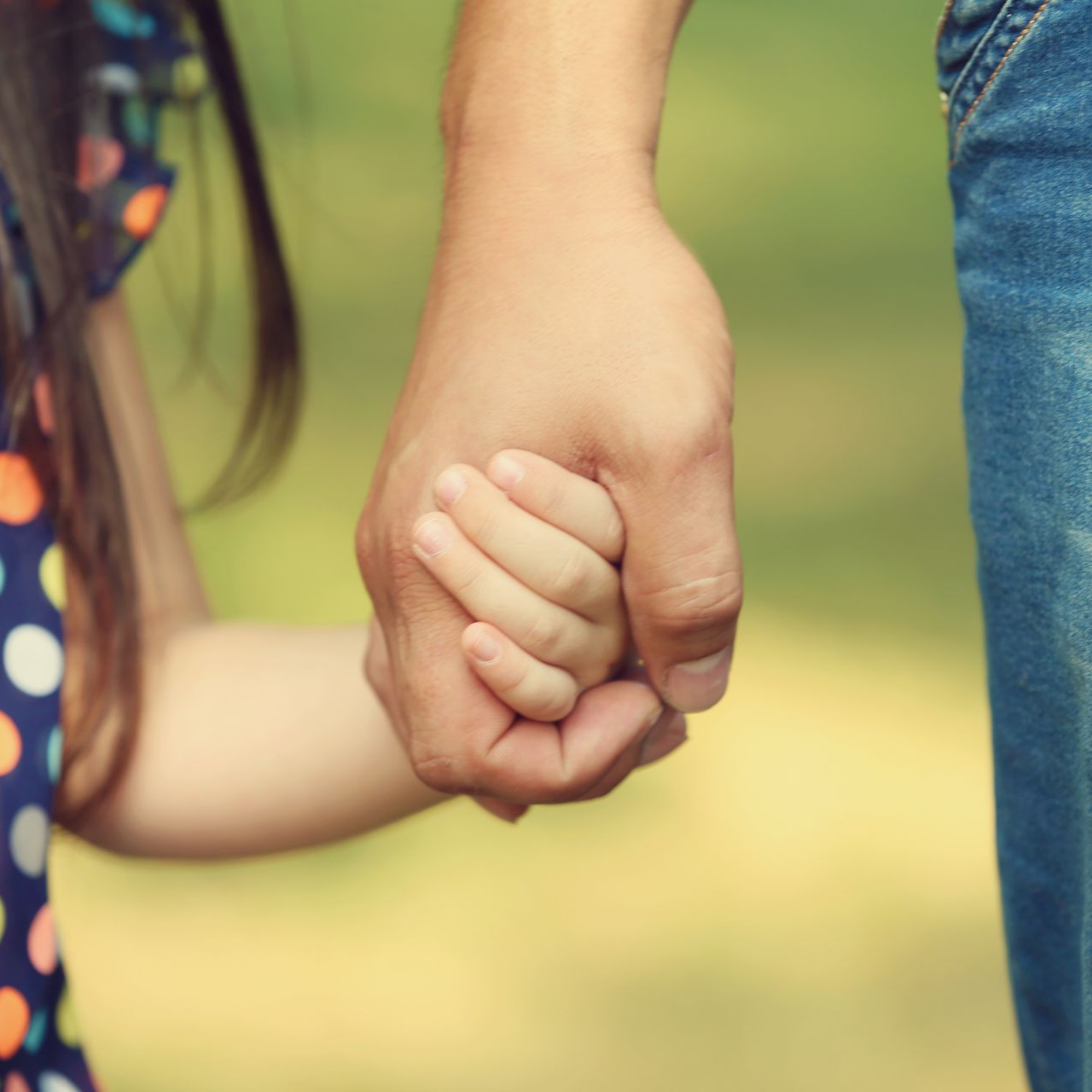 Main d'adulte tenant la main d'un enfant. Teint clair. Fond vert flou.