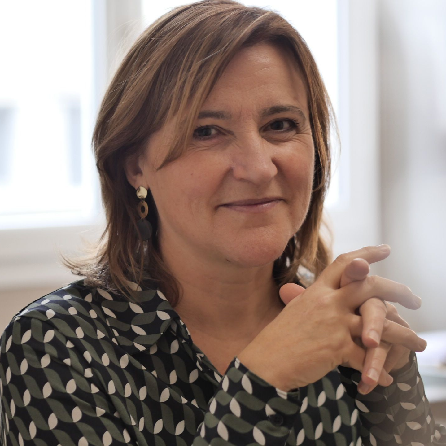 Femme les mains jointes, vêtue d'un haut à motifs, regardant l'objectif.