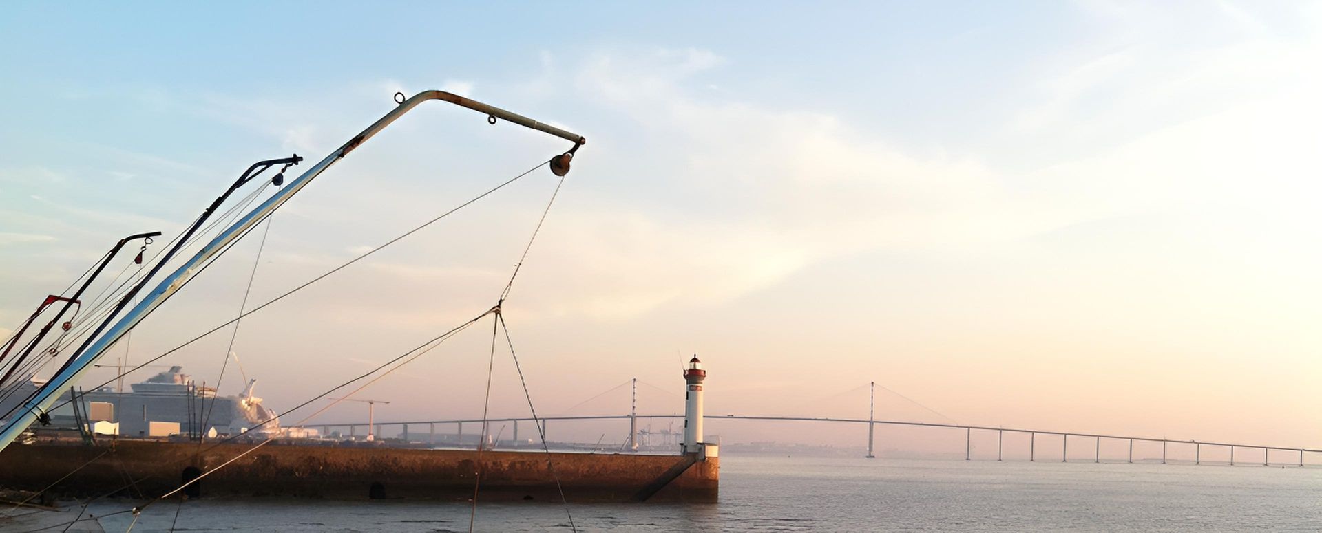 Scène portuaire avec de grandes grues de pêche, un phare et une jetée à l'aube.