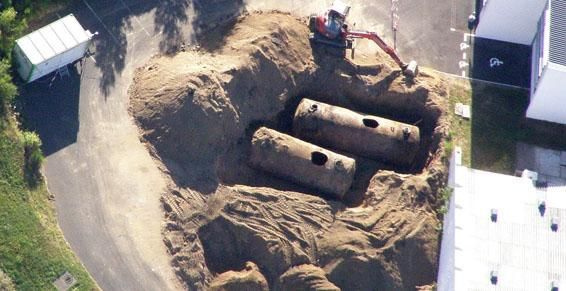 Deux réservoirs cylindriques dans une fosse à terre, une excavatrice à proximité. Chantier de construction.