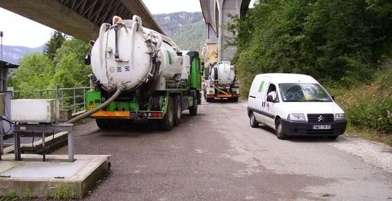 Deux camions-citernes et une camionnette blanche sur une route sous un pont, un camion vert est en train de livrer.