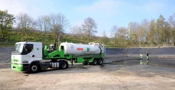 Un camion-citerne blanc et vert pompe un liquide d'une fosse étanche en milieu rural.