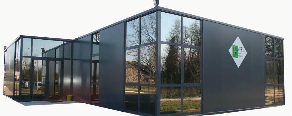 Un bâtiment moderne gris, avec des murs de verre et un logo vert.