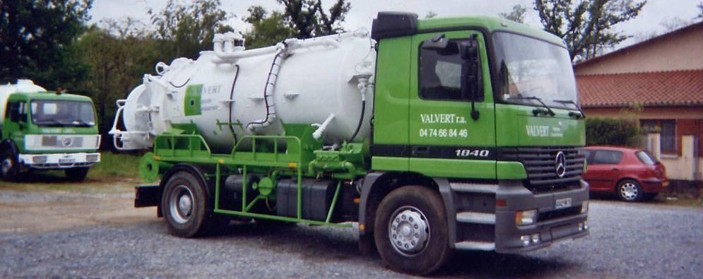 Deux camions de ramassage verts sur un terrain gravillonné ; l'un d'eux est équipé d'une grande citerne blanche.