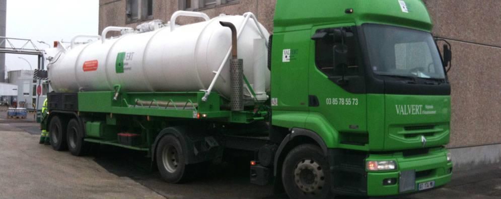 Camion-citerne vert stationné devant un bâtiment.