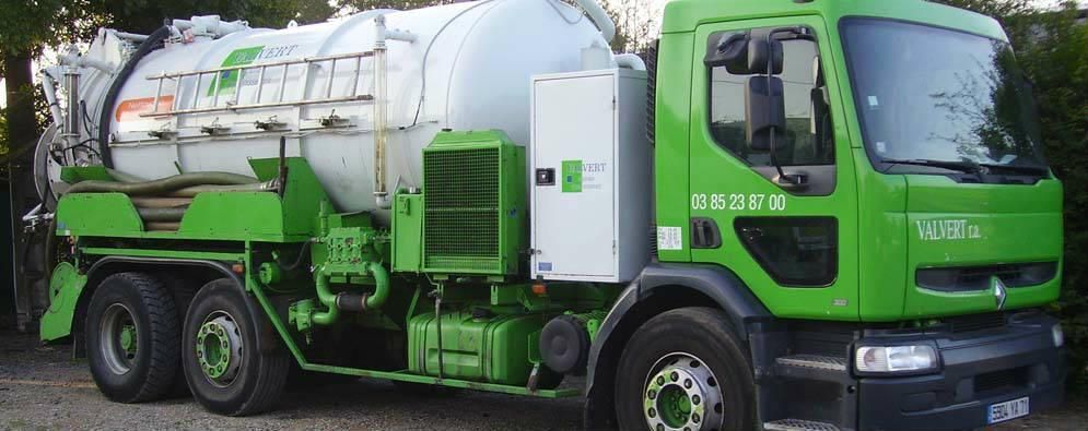 Camion aspirateur vert et blanc stationné sur la route.