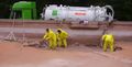 Des ouvriers en combinaisons jaunes pelletent de la boue dans un camion aspirateur.