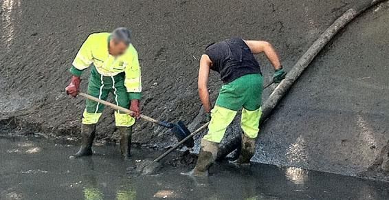 Deux ouvriers en tenue de travail nettoient un fossé boueux à la pelle.