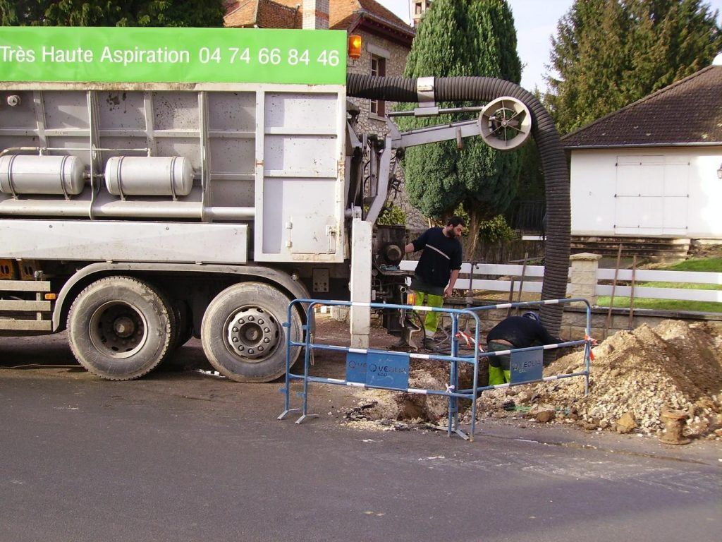 Un gros camion aspirateur avec des ouvriers en train d'extraire des débris d'une route.