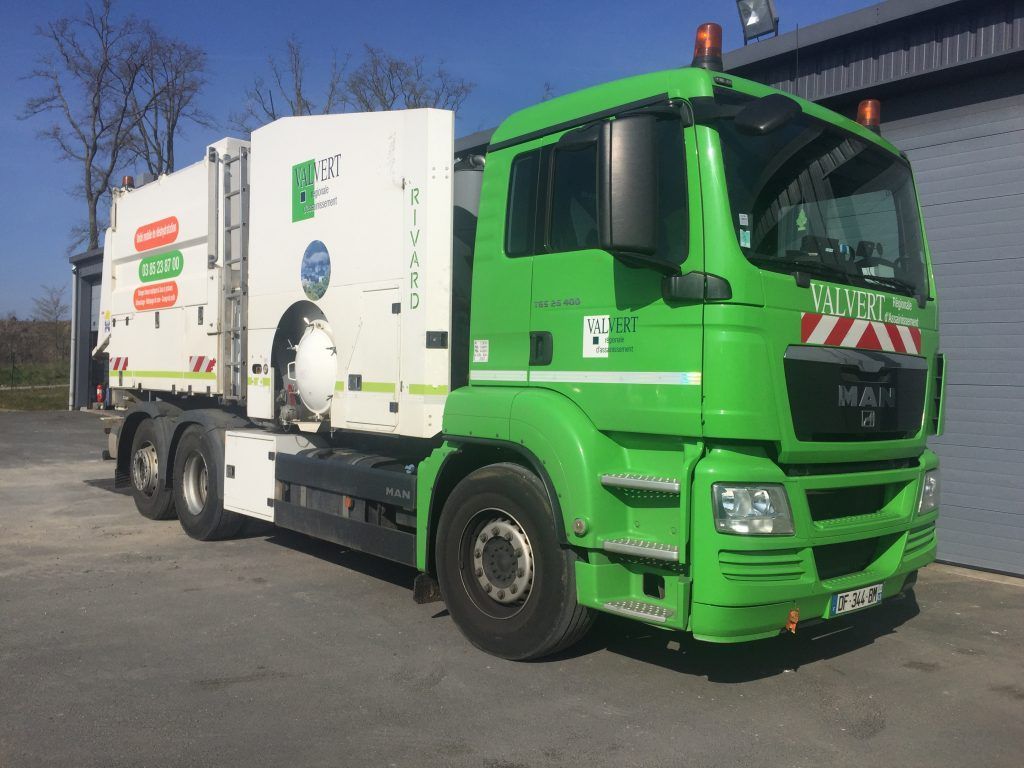 Camion-poubelle vert stationné devant un bâtiment.