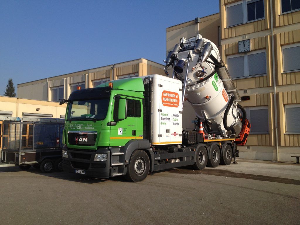 Un camion MAN vert transportant un gros composant industriel blanc devant un bâtiment.
