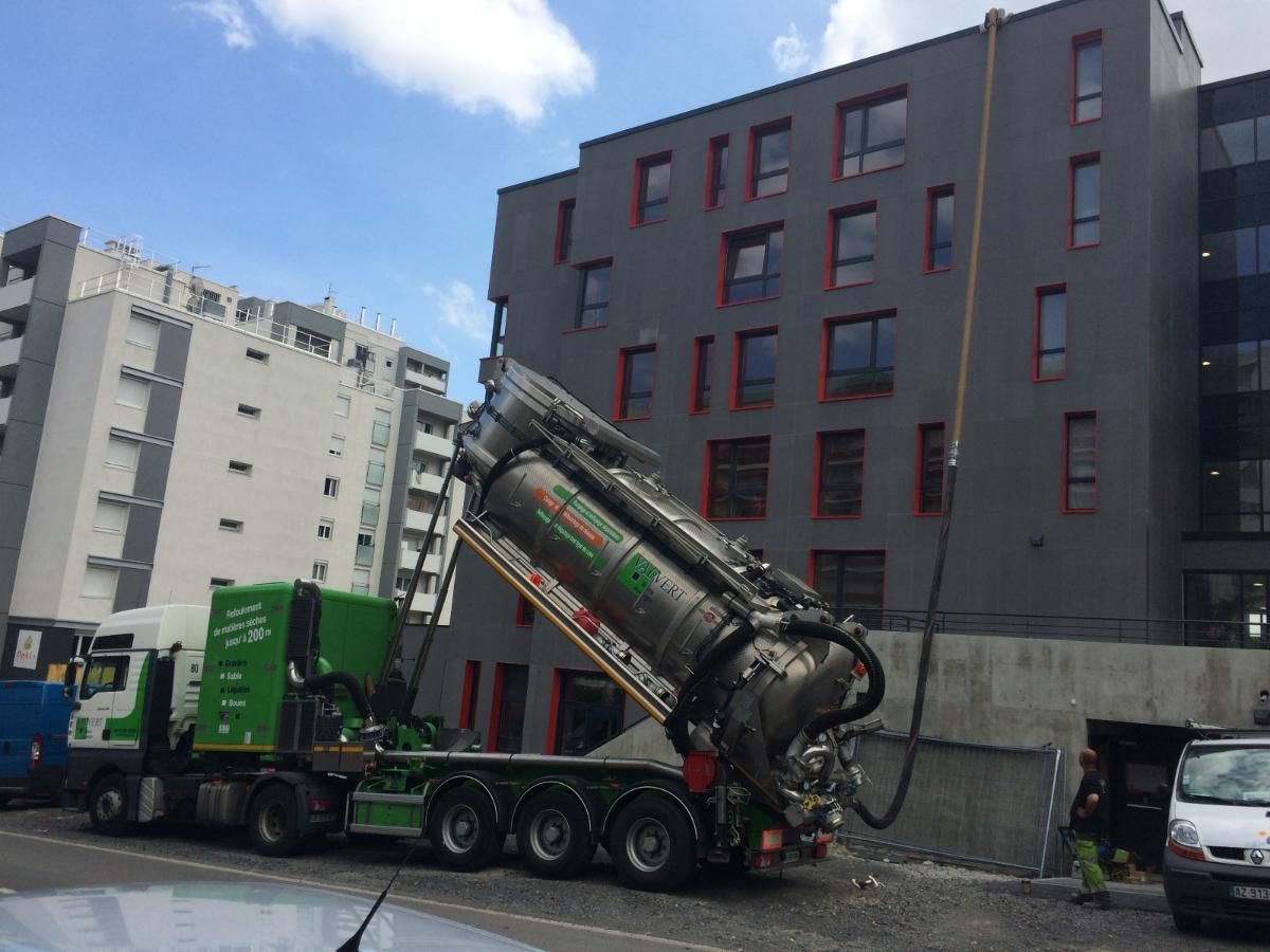 Un gros camion-benne vert et argenté, sa citerne levée, est garé à côté d'un bâtiment moderne.