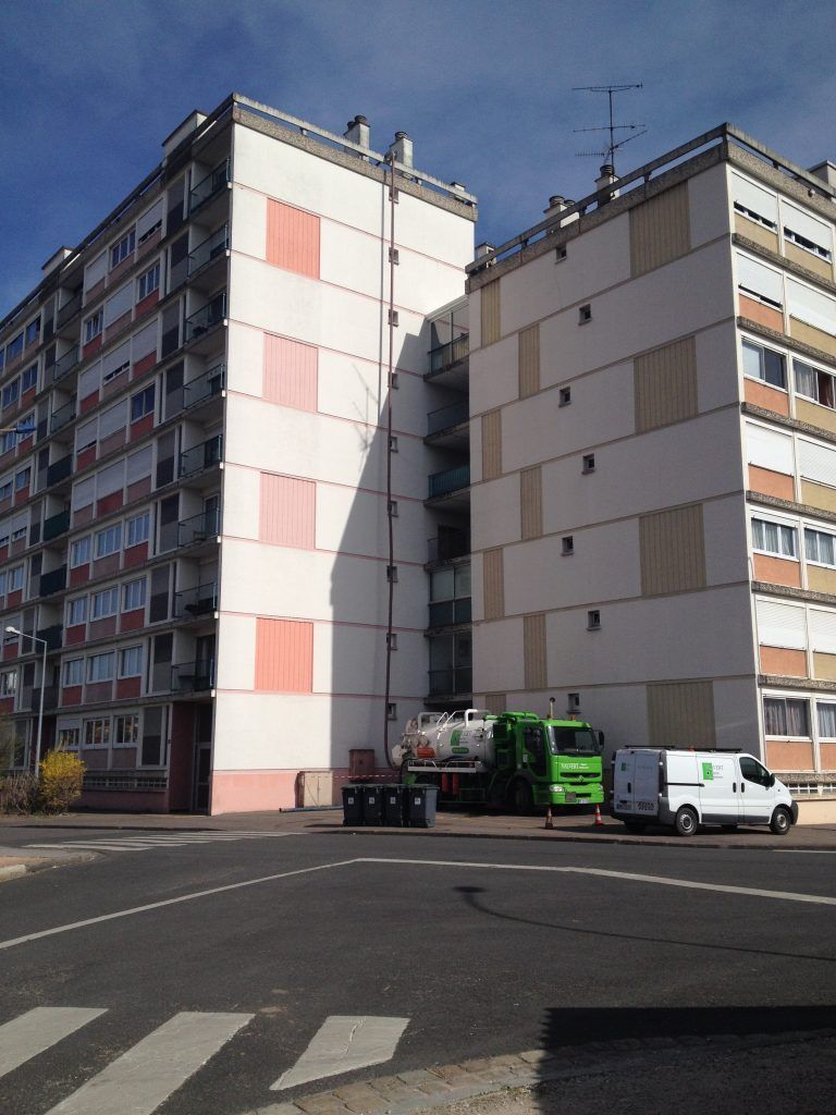 Immeubles d'appartements avec véhicules de service stationnés à un coin de rue sous un ciel bleu.