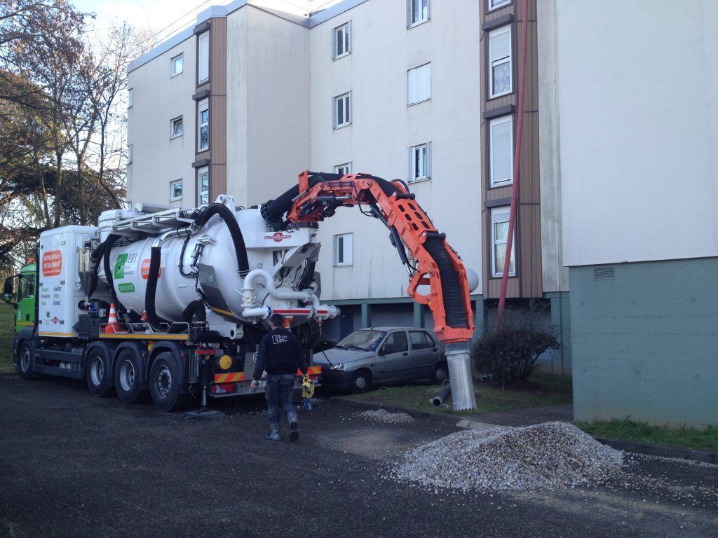 Un gros camion équipé d'un bras articulé extrait des débris près d'un bâtiment.