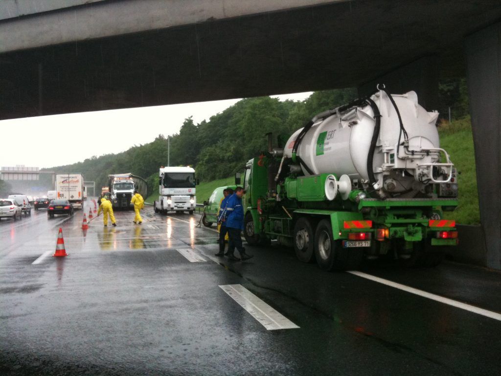 Un gros camion vert équipé d'une citerne est coincé sous un pont, la circulation est ralentie et des ouvriers sont sur place.