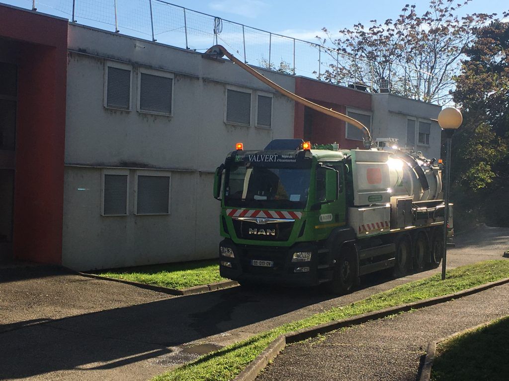 Camion vert muni d'un long tuyau nettoyant le toit d'un bâtiment.