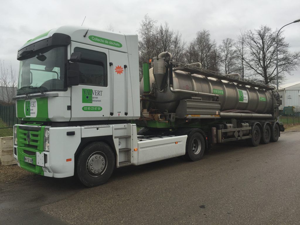 Camion-citerne blanc et vert stationné sur une route, journée nuageuse.