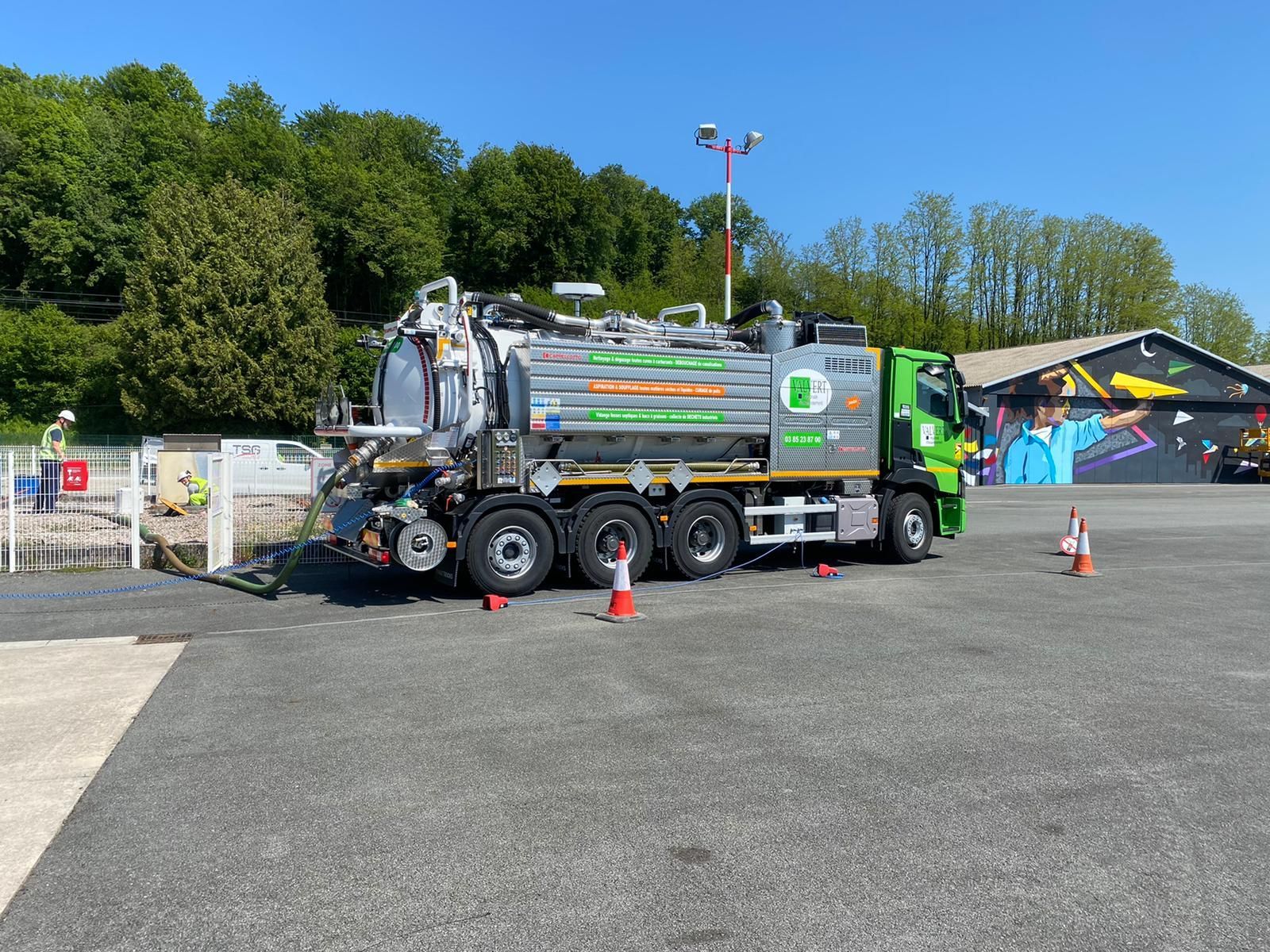 Camion vert et blanc, service d'entretien des égouts. Des ouvriers en gilets haute visibilité raccordent du matériel à une bouche d'égout.