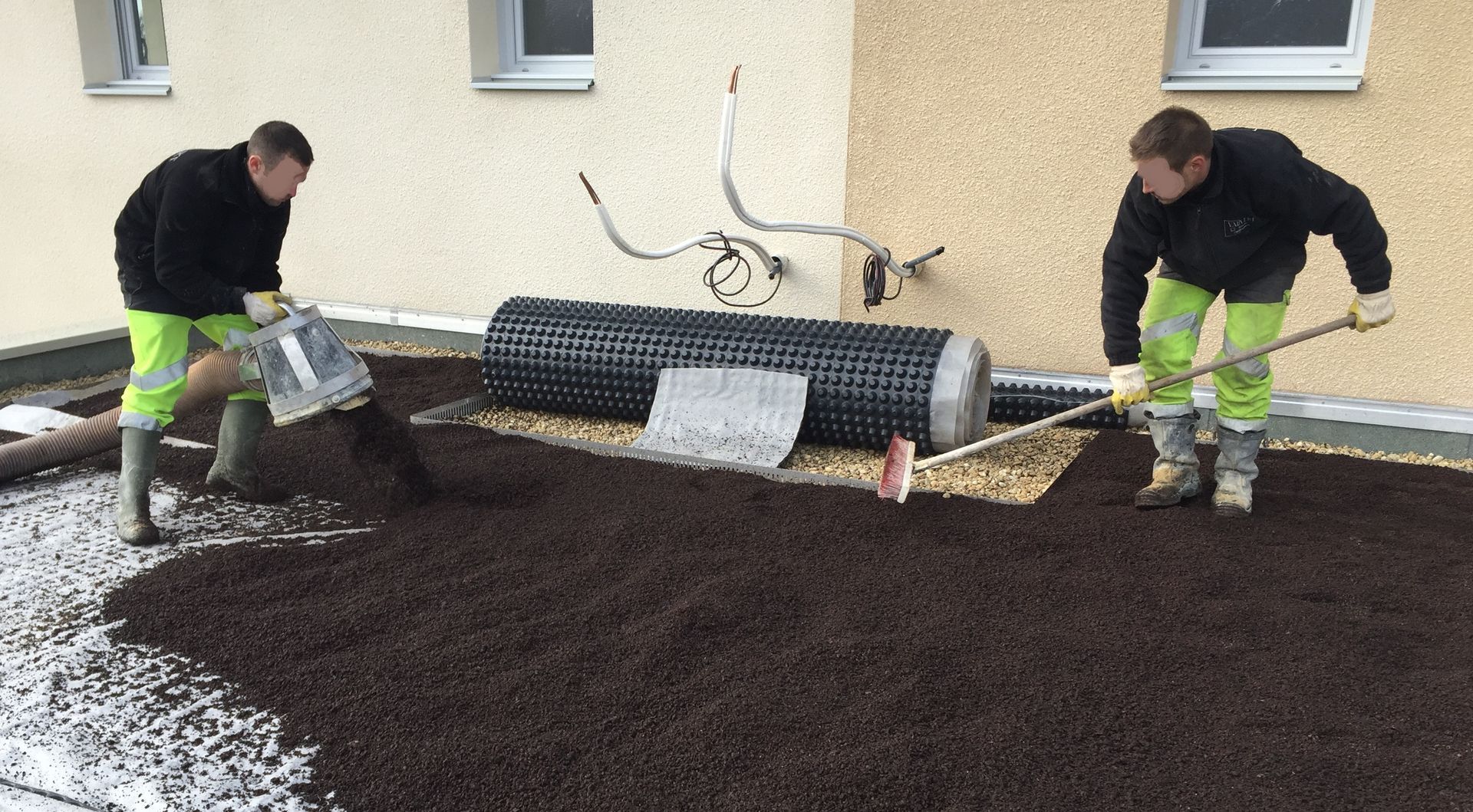 Un camion-citerne vert et argenté vide sa cuve dans un tuyau près d'un bâtiment. Un ouvrier en jaune se tient à proximité.