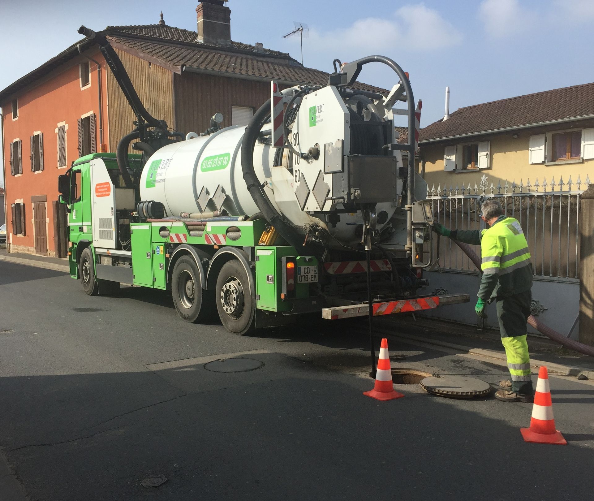 Un camion-poubelle vert et blanc est stationné devant un bâtiment gris par une journée ensoleillée.