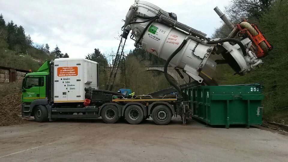 Un camion vert vide un grand conteneur blanc dans une benne à ordures verte à l'extérieur.
