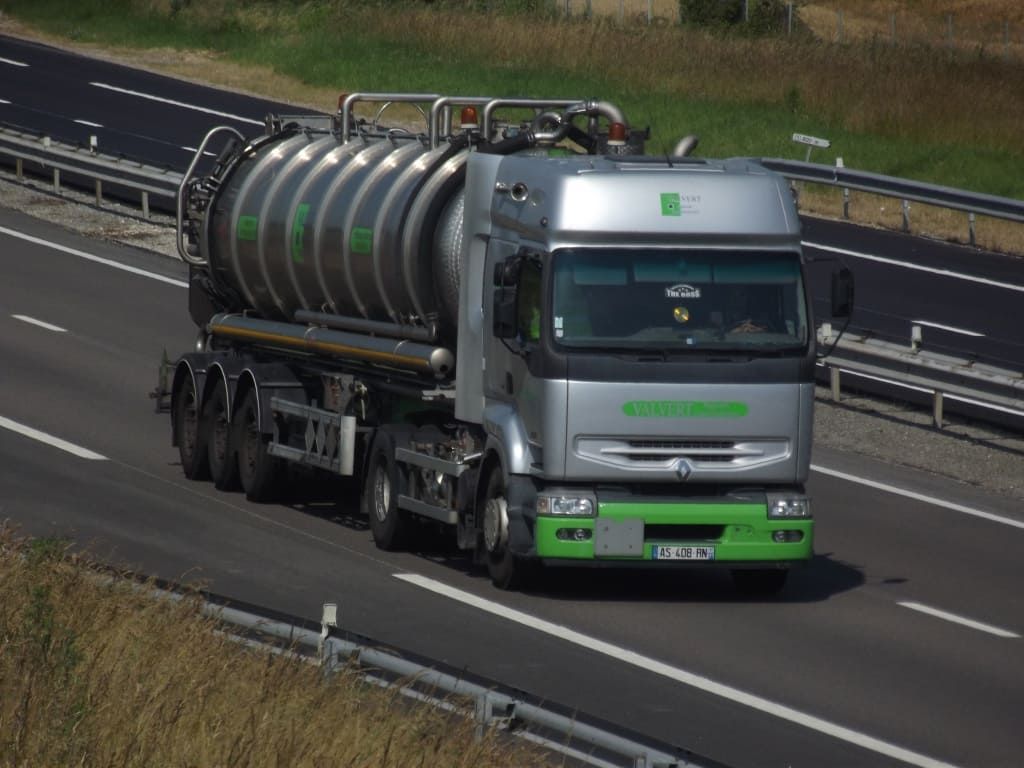 Camion-citerne circulant sur une autoroute, gris avec des touches de vert, en journée.