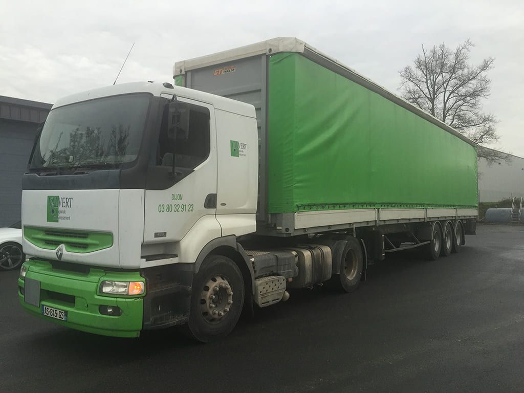 Un semi-remorque blanc et vert avec une remorque verte est garé à l'extérieur.