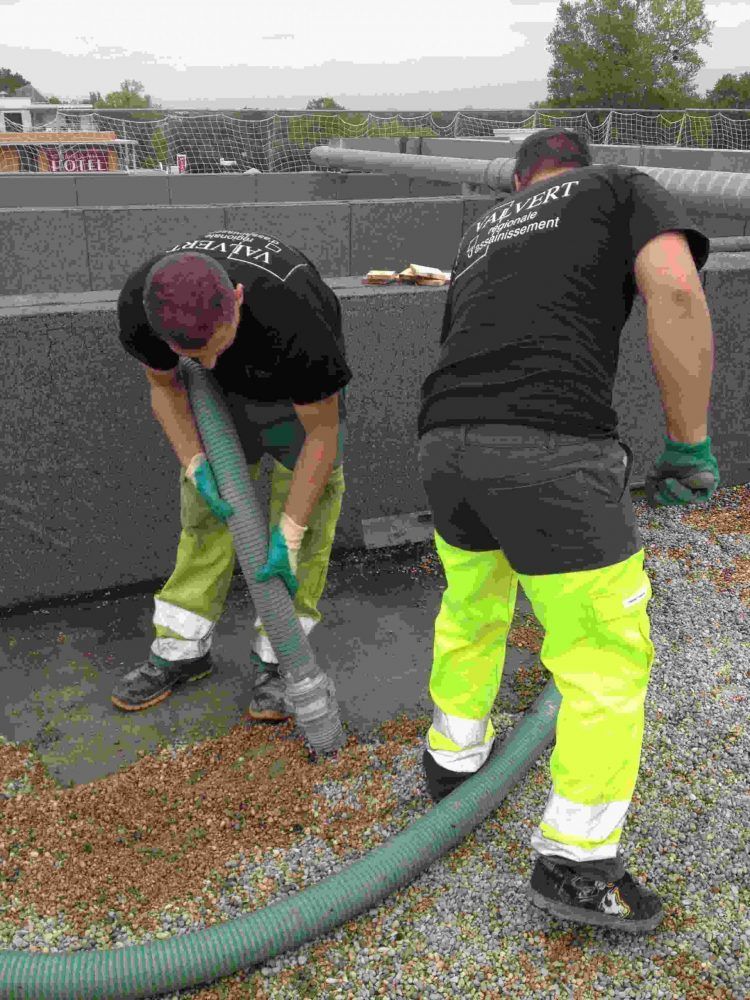 Deux ouvriers en tenue de sécurité utilisent un tuyau d'arrosage sur une surface en béton.