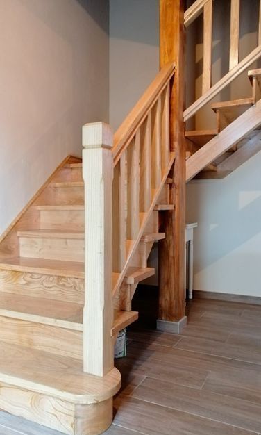 Escalera de madera con barandillas de madera clara y postes blancos en el interior de una vivienda.