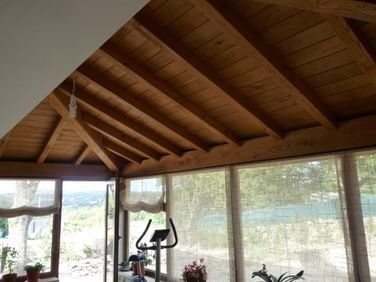 Cenador de madera con techo abovedado, grandes ventanales y una bicicleta estática en el interior con vistas panorámicas.