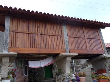 Casa rústica de piedra de dos plantas con balcón de madera y flores rojas bajo el alero.