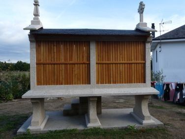 Pequeño santuario de madera sobre una plataforma de hormigón con pilares de piedra, al aire libre bajo un cielo nublado.