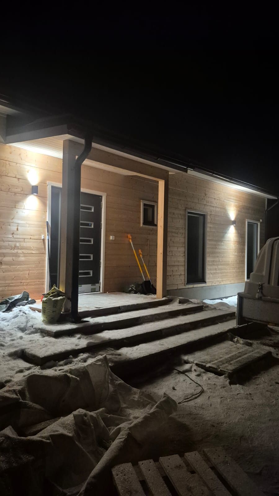 Tiilitalon luminen kuisti yöllä, kuistivalon ja valosarjavalojen valaistuna.