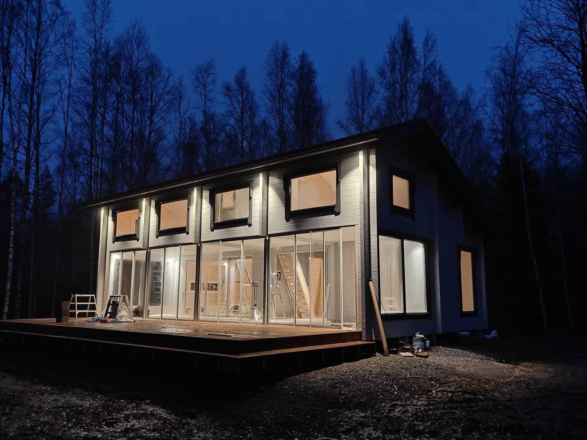 Moderni kaksikerroksinen talo lämpimillä valoilla ja suurilla ikkunoilla pimeässä metsäisessä ympäristössä yöllä