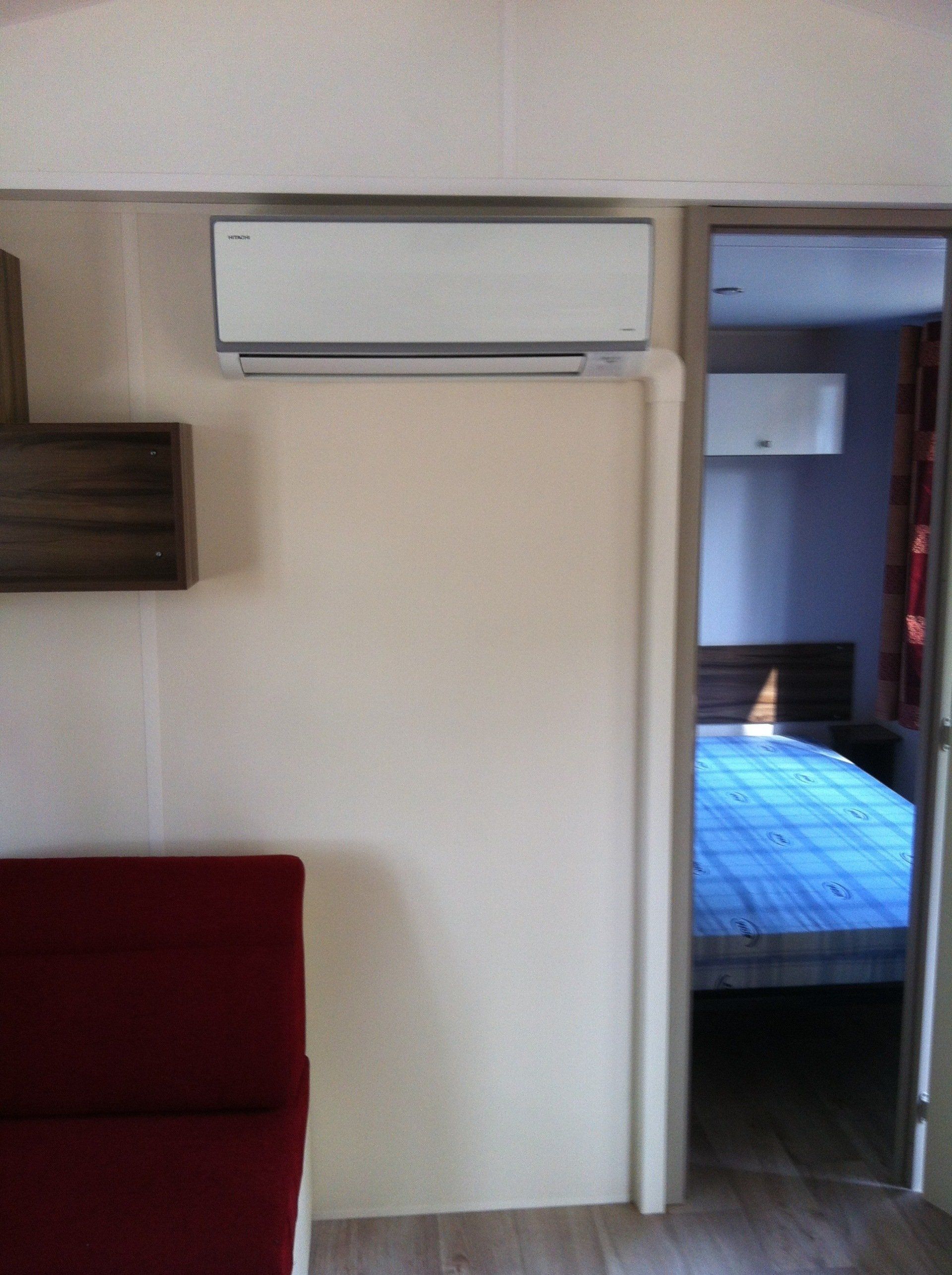 Petite pièce avec climatiseur mural, porte donnant sur la chambre et bord de canapé rouge au premier plan.