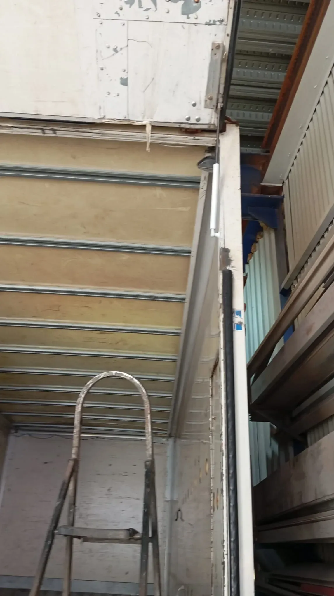 Escalera apoyada contra una pared; una sección del techo y una pared lateral están expuestos.